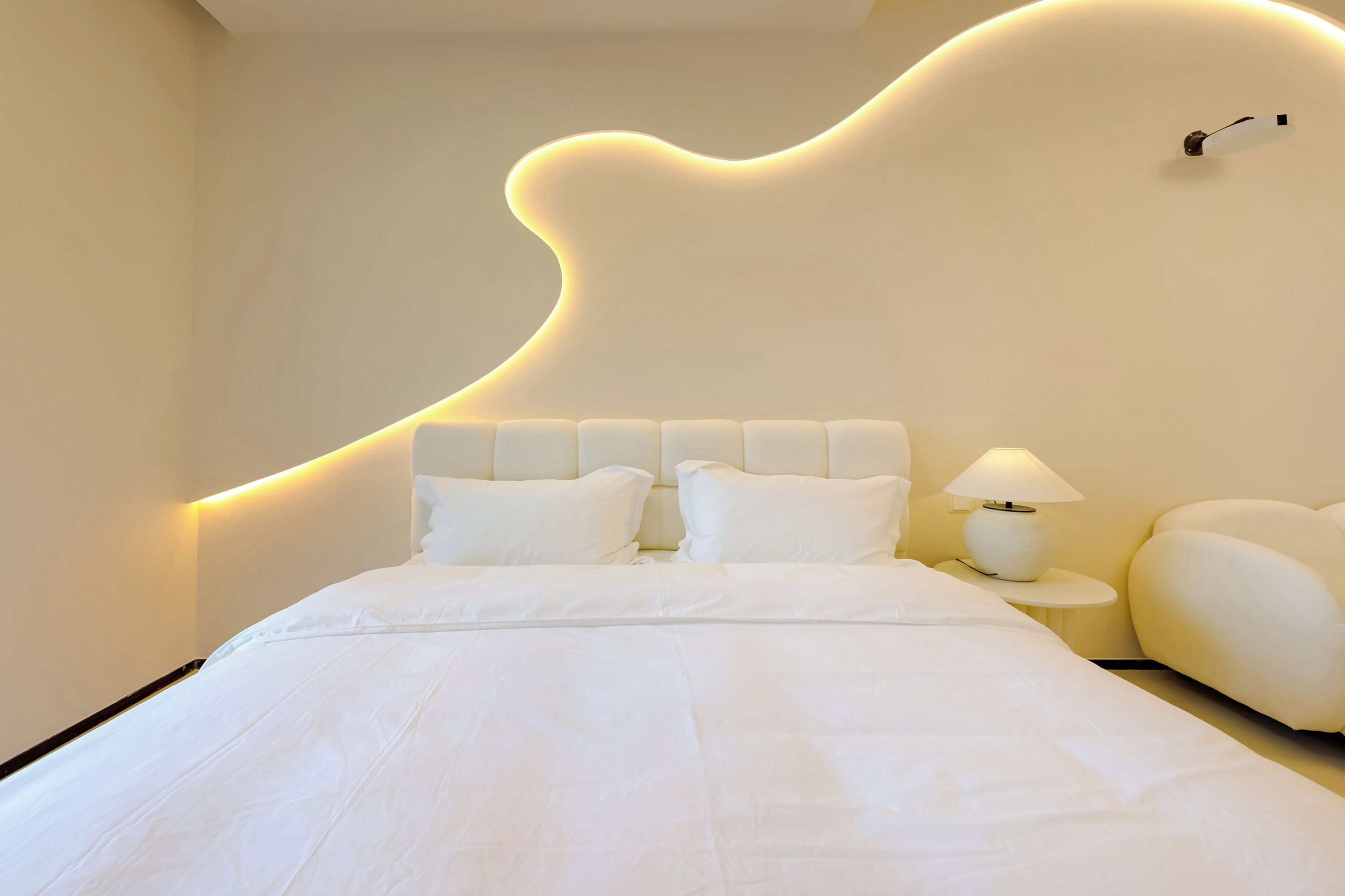 Un dormitorio moderno con una cama grande, una mesita de noche con lámpara y un diseño de pared original.