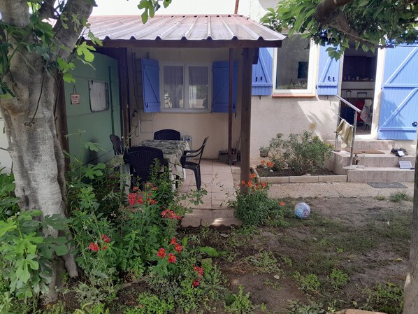 A small outdoor patio with a table and chairs, surrounded by plants and a garden.