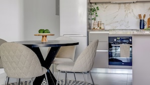 A modern kitchen with a white refrigerator, a marble backsplash, and a built-in oven. There is a dining table with two chairs and a small plant on the counter. - Sanders Triple Limassol (Limassol)