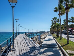 A wooden boardwalk by the sea with street lamps and palm trees. - Sanders Triple Limassol (Limassol)