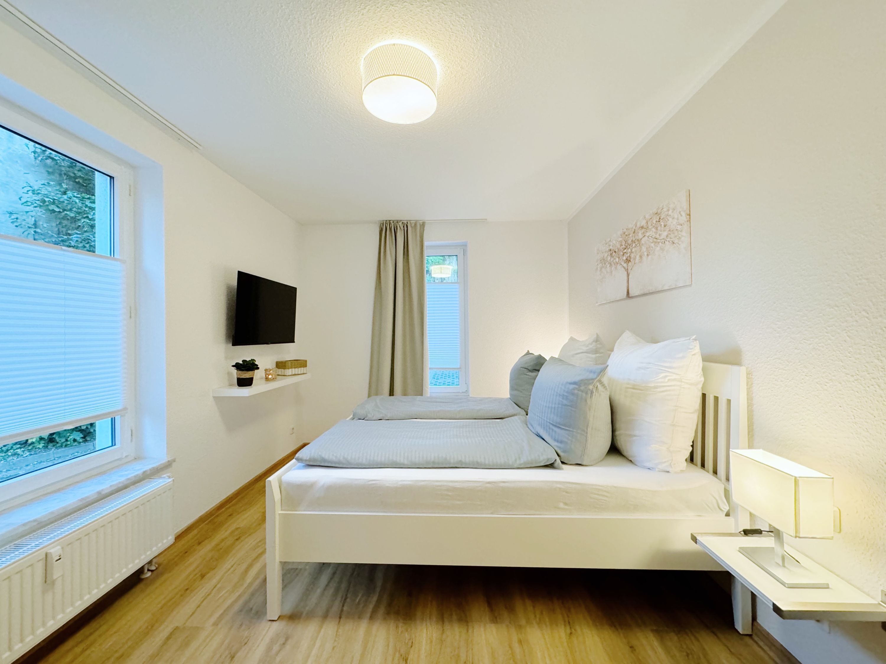 Une chambre moderne avec un lit, une télévision, une table de chevet et une fenêtre avec des stores.