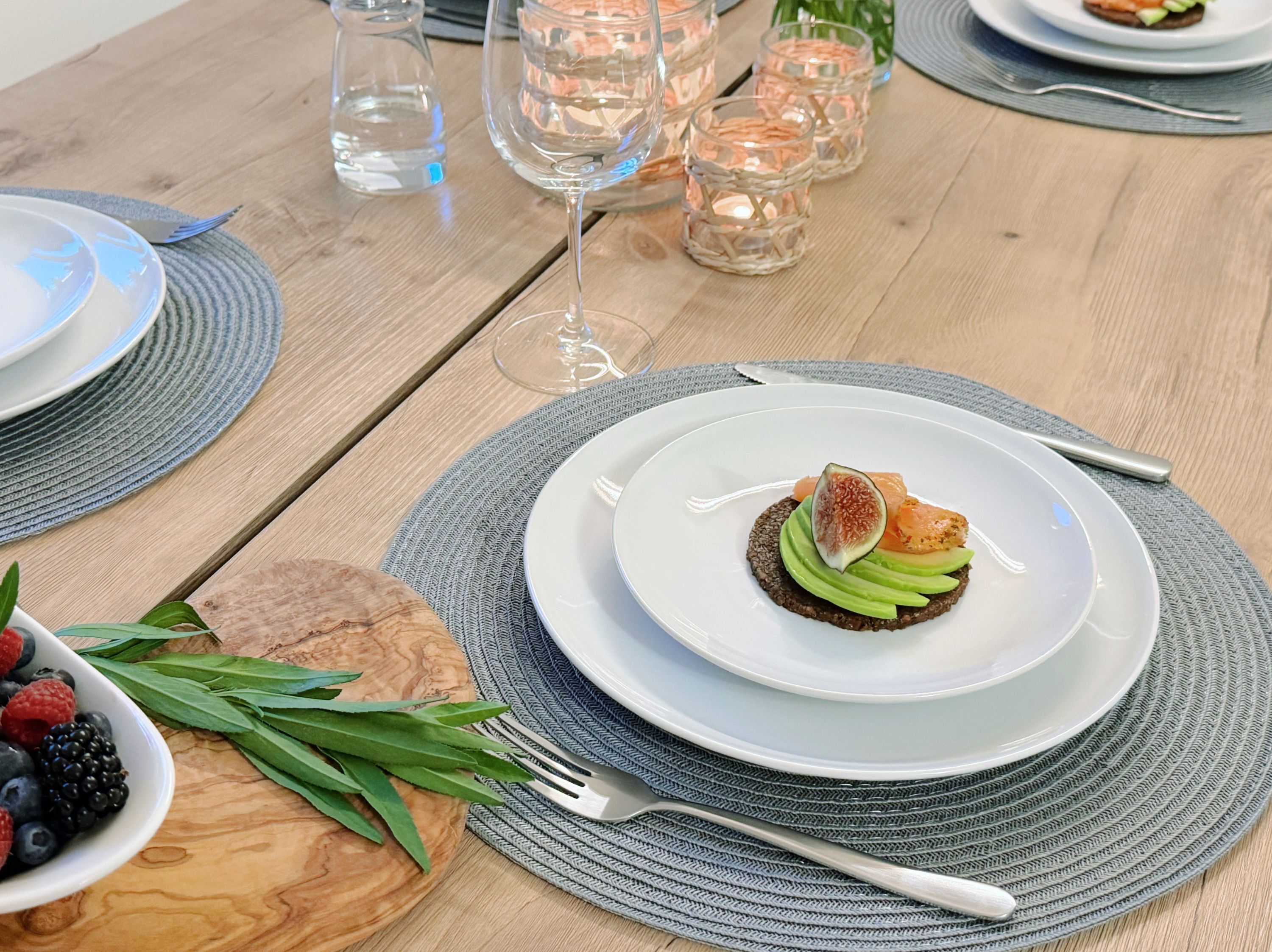 A wooden table with a white plate of food, a bowl of berries, and a glass of water.