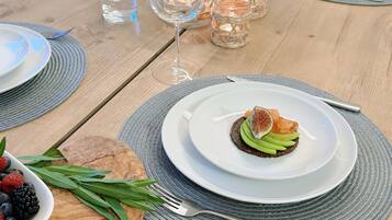 A wooden table with a white plate of food, a bowl of berries, and a glass of water.
