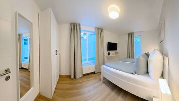 A bedroom with a bed, a TV mounted on the wall, and a window with curtains.