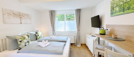 A hotel room with two beds, a desk with a chair, a television, and a window with curtains.