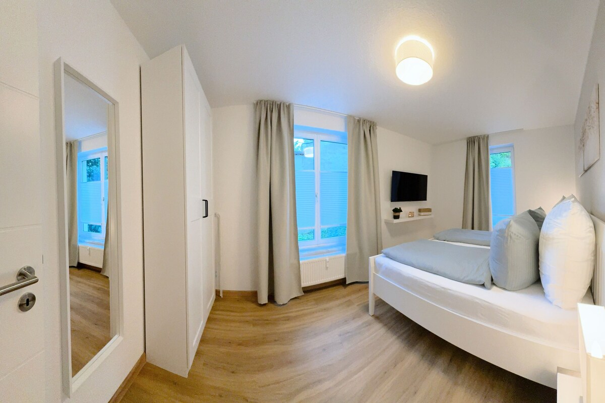 A bedroom with a bed, a TV mounted on the wall, and a window with curtains.