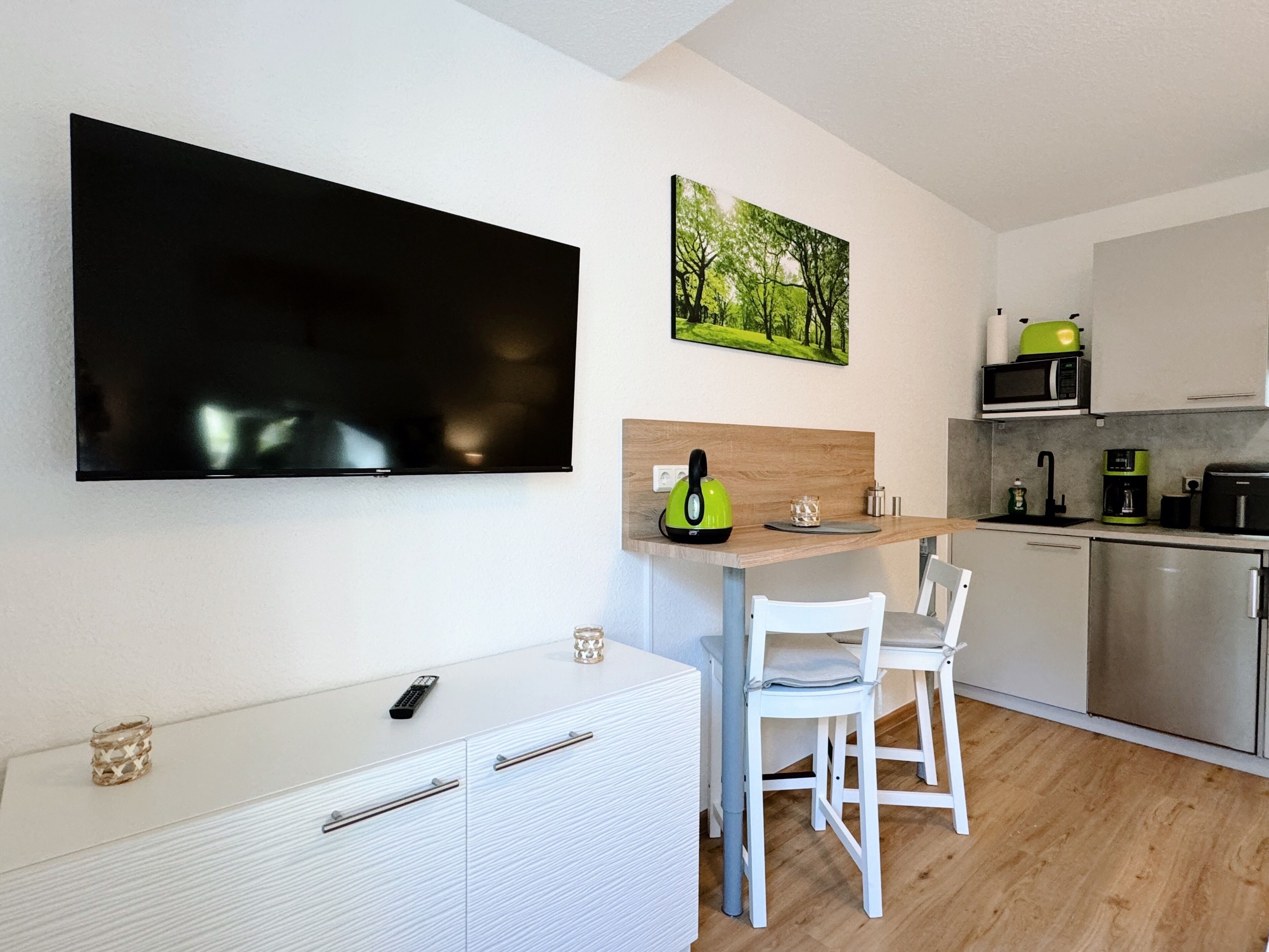 A modern kitchen with a flat-screen TV, a painting, and a kettle on the counter.