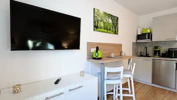 A modern kitchen with a flat-screen TV, a painting, and a kettle on the counter.