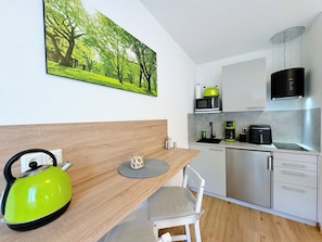 A modern kitchen with a dining table, chairs, a kettle, a sink, a microwave, a coffee maker, and cabinets. - REGIOHOTEL Harzresidenz (Wernigerode)