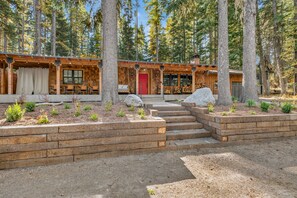 Une cabane au revêtement extérieur en bois, avec une porte rouge et un chemin de pierres menant à l’entrée.