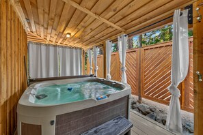 Un bain à remous sous une pergola en bois, avec une clôture en bois en arrière-plan.