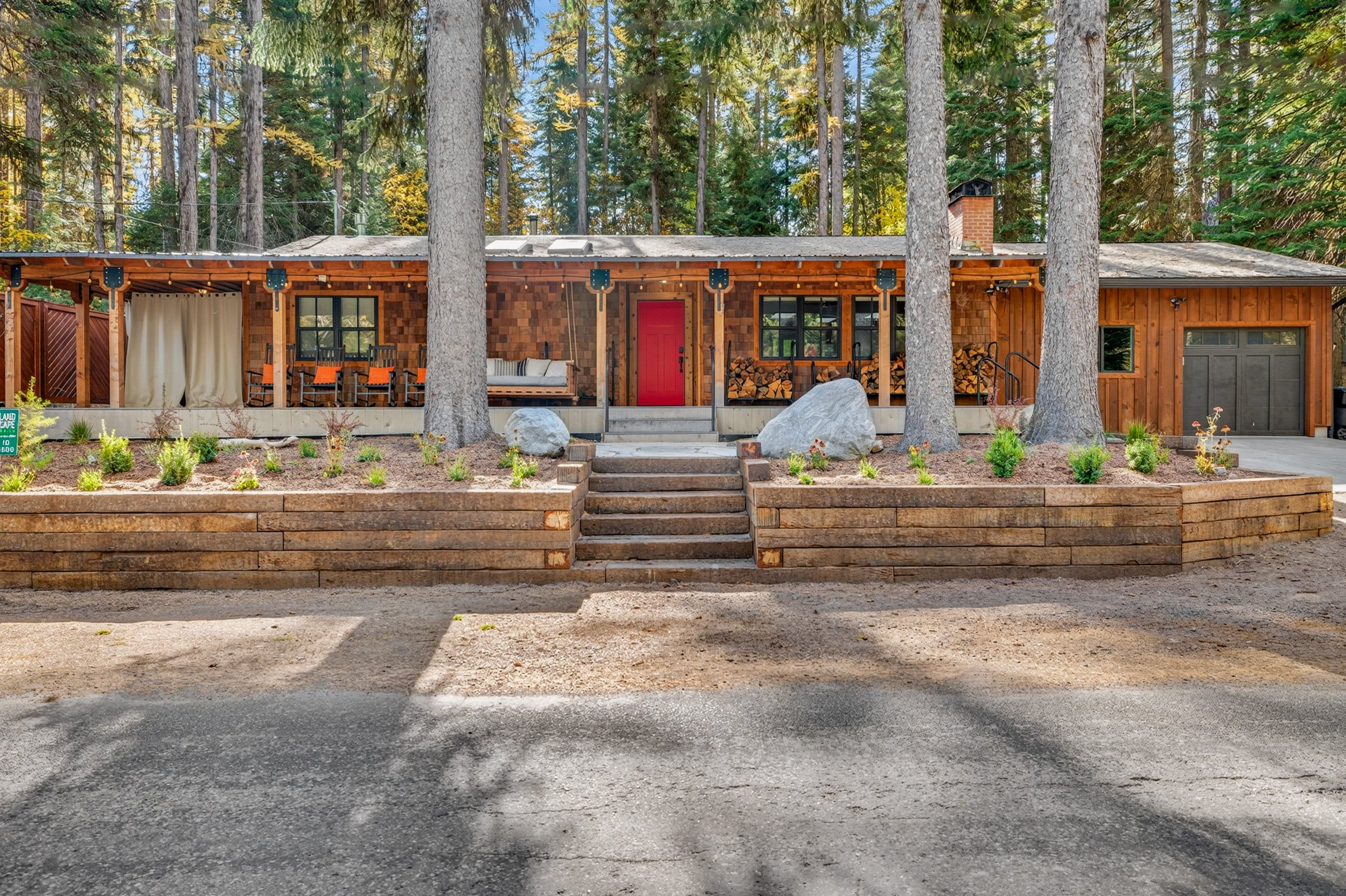 A cabin with a porch, a red door, and a covered seating area with chairs.