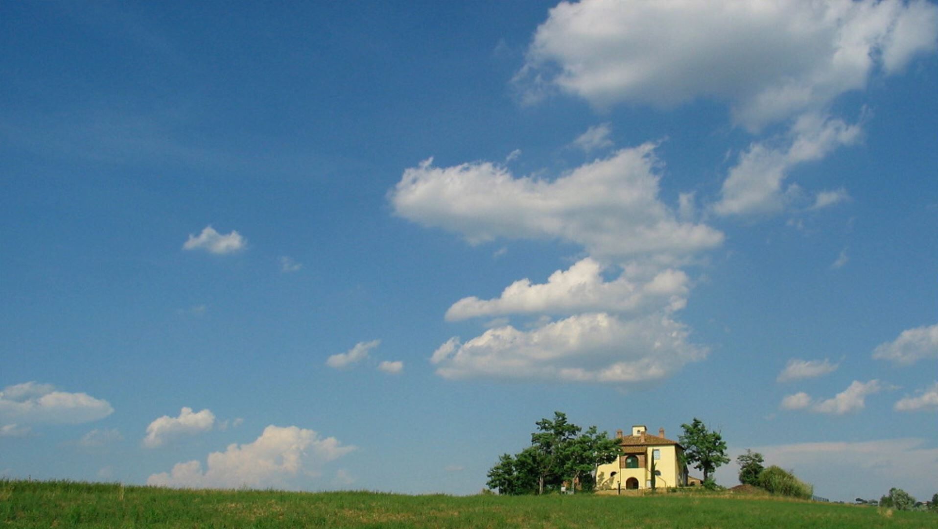 A single-story building with a flat roof, surrounded by a grassy field and a few trees.