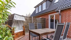 En terrasse med et træbord og stole, et overdækket siddeområde og en murstensmur.