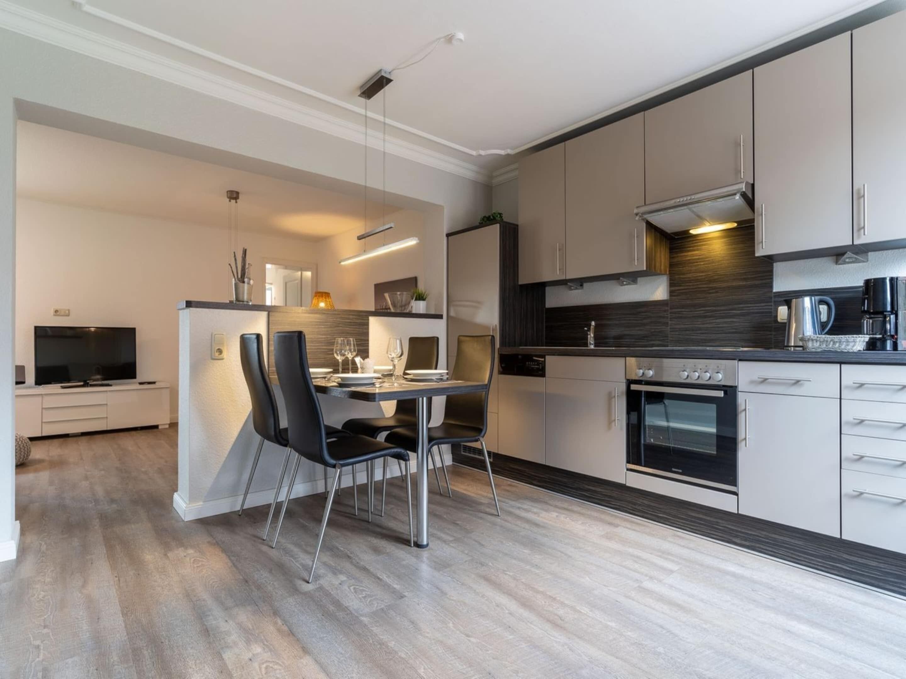 A modern kitchen with a dining area, built-in appliances, and a flat-screen TV.