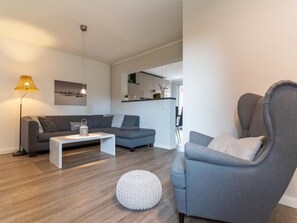 A modern living room with a grey sofa, a white coffee table, and a grey armchair. There is a round white pouf on the floor. - Ferienwohnung Lieblingsmeer (St. Peter-Ording)