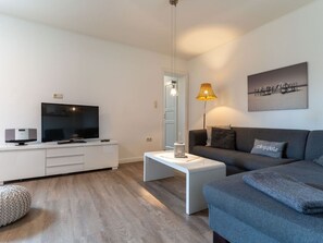 A modern living room with a flat-screen TV, a white coffee table, a grey sofa, and a lamp. - Ferienwohnung Lieblingsmeer (St. Peter-Ording)