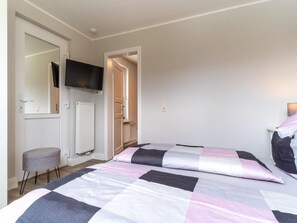 A bedroom with a bed, a television mounted on the wall, a radiator, and a door leading to another room. - Ferienwohnung Lieblingsmeer (St. Peter-Ording)