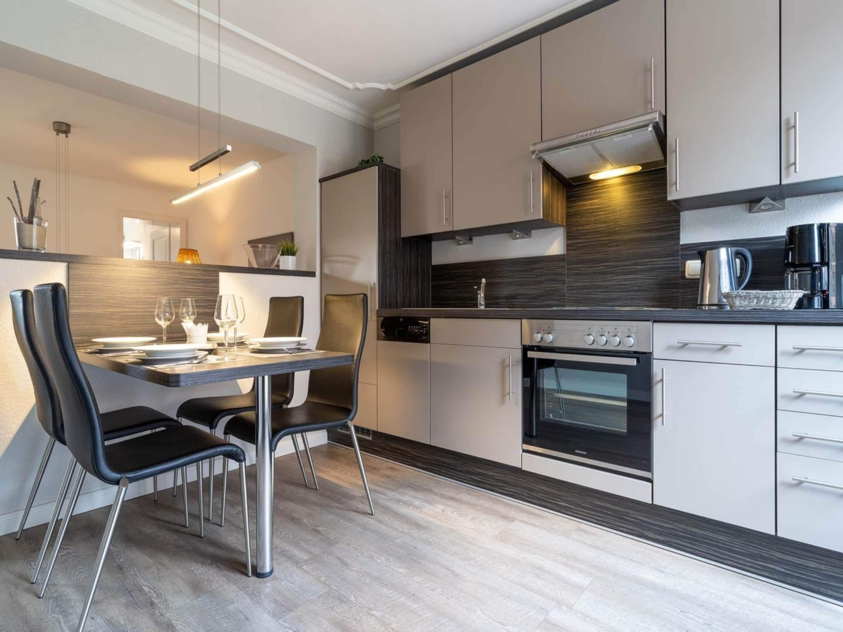 A modern kitchen with a dining area, featuring a built-in oven, a coffee maker, and a dining table with chairs.