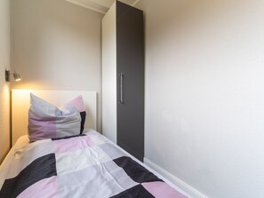 A bedroom with a bed, a bedside lamp, a wardrobe, and a wall-mounted light fixture. - Ferienwohnung Lieblingsmeer (St. Peter-Ording)