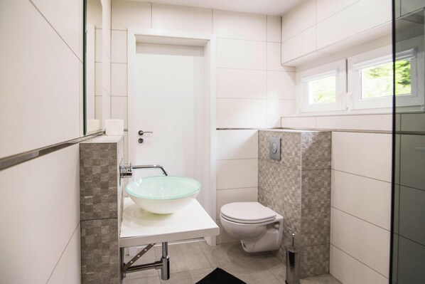 A bathroom with a glass bowl sink, a toilet, and a shower area. - Holiday Home With Garden, Close to the Lake (Dąbrówno)