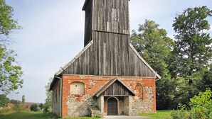 Una iglesia de madera rústica con base de ladrillo, un alto campanario y una entrada sencilla.