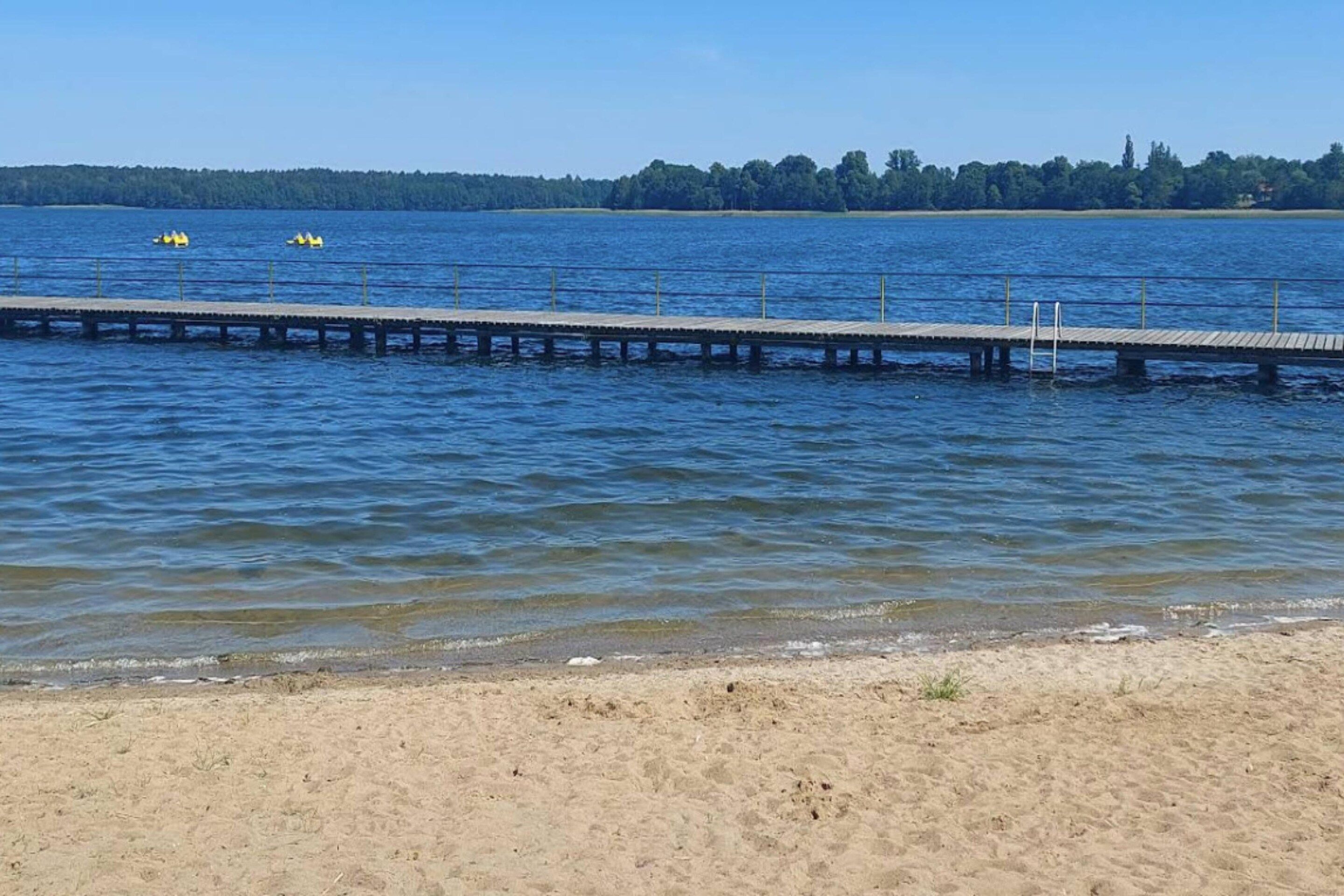 Une longue jetée s’étendant dans une étendue d’eau calme, avec une plage de sable au premier plan.