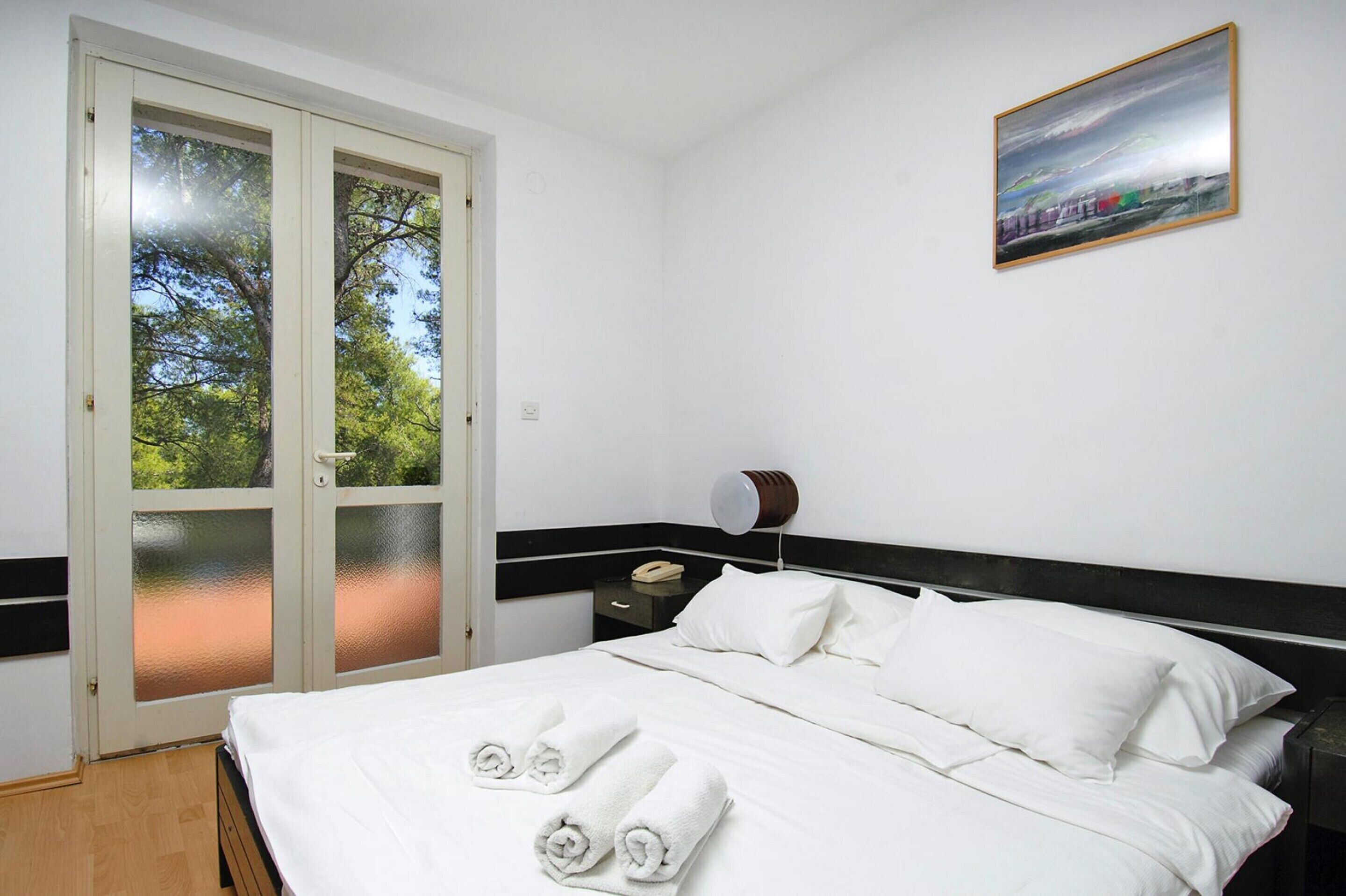 Una habitación de hotel con una cama, ropa de cama blanca, una mesita de noche, una lámpara y un cuadro en la pared.