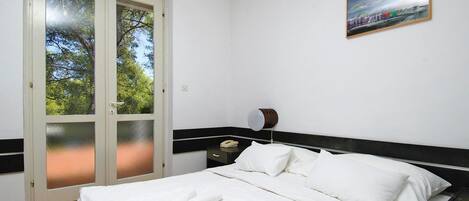 Una habitación de hotel con una cama, ropa de cama blanca, una mesita de noche, una lámpara y un cuadro en la pared.