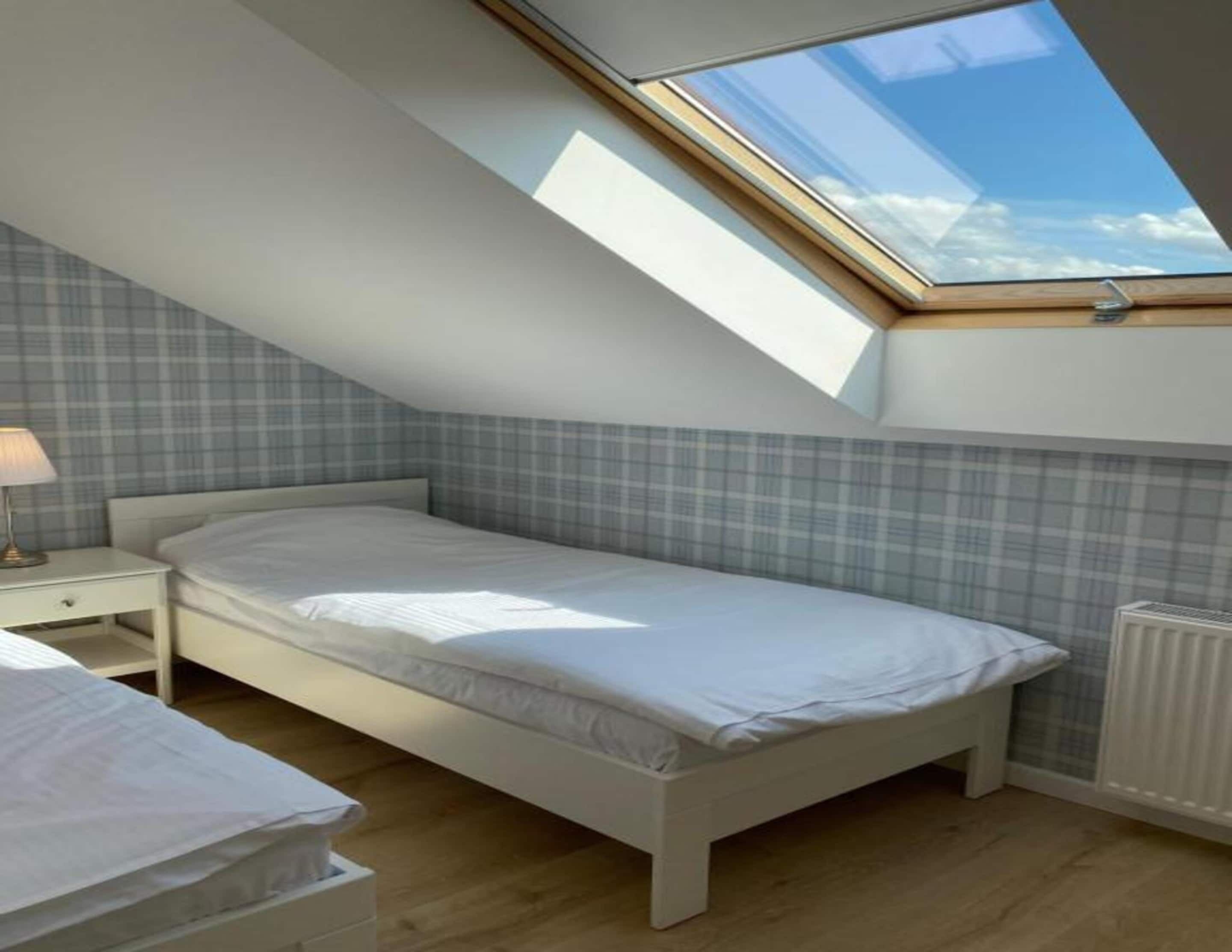 A bedroom with a skylight, a bed, a bedside table, and a radiator.