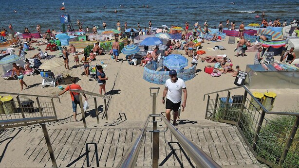 Una playa concurrida, gente, sombrillas y sillas de playa.