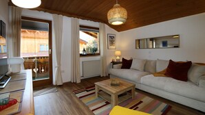 Een woonkamer met een houten plafond, een bank, een salontafel, een lamp en uitzicht door een raam.