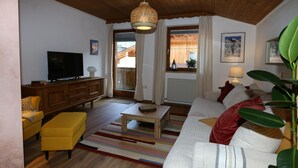Een woonkamer met een televisie, bank, voetenbankje, salontafel en een hanglamp.