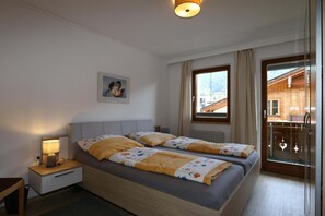 A bedroom with two beds, a nightstand, a lamp, a window with a view of a wooden cabin, and a door with glass panels. - Holiday Home, Axams (Axams)