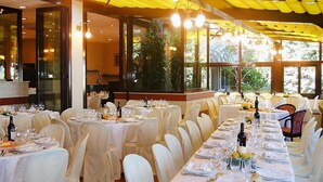 Un'elegante sala da pranzo con diversi tavoli apparecchiati, ampie finestre e un soffitto giallo.