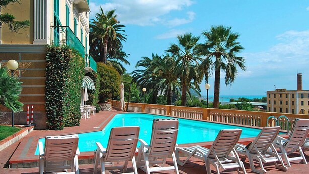 Area piscina con sedie a sdraio, piscina e vista sul mare.