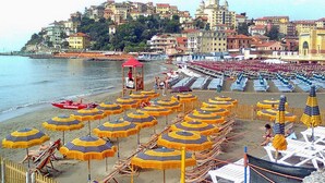 Una spiaggia con file di ombrelloni gialli e blu a righe, lettini e una torretta di salvataggio.