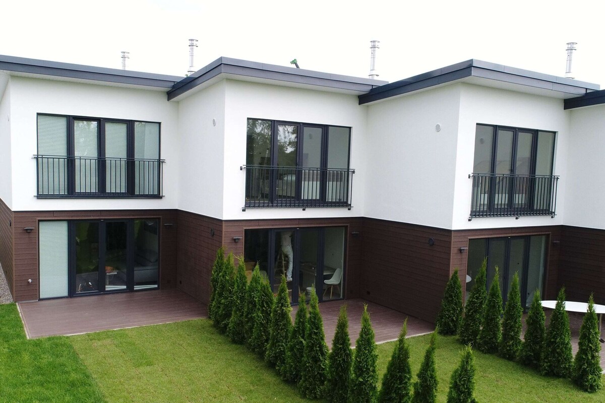 A modern two-story residential building with large windows, a covered patio, and a well-maintained lawn.