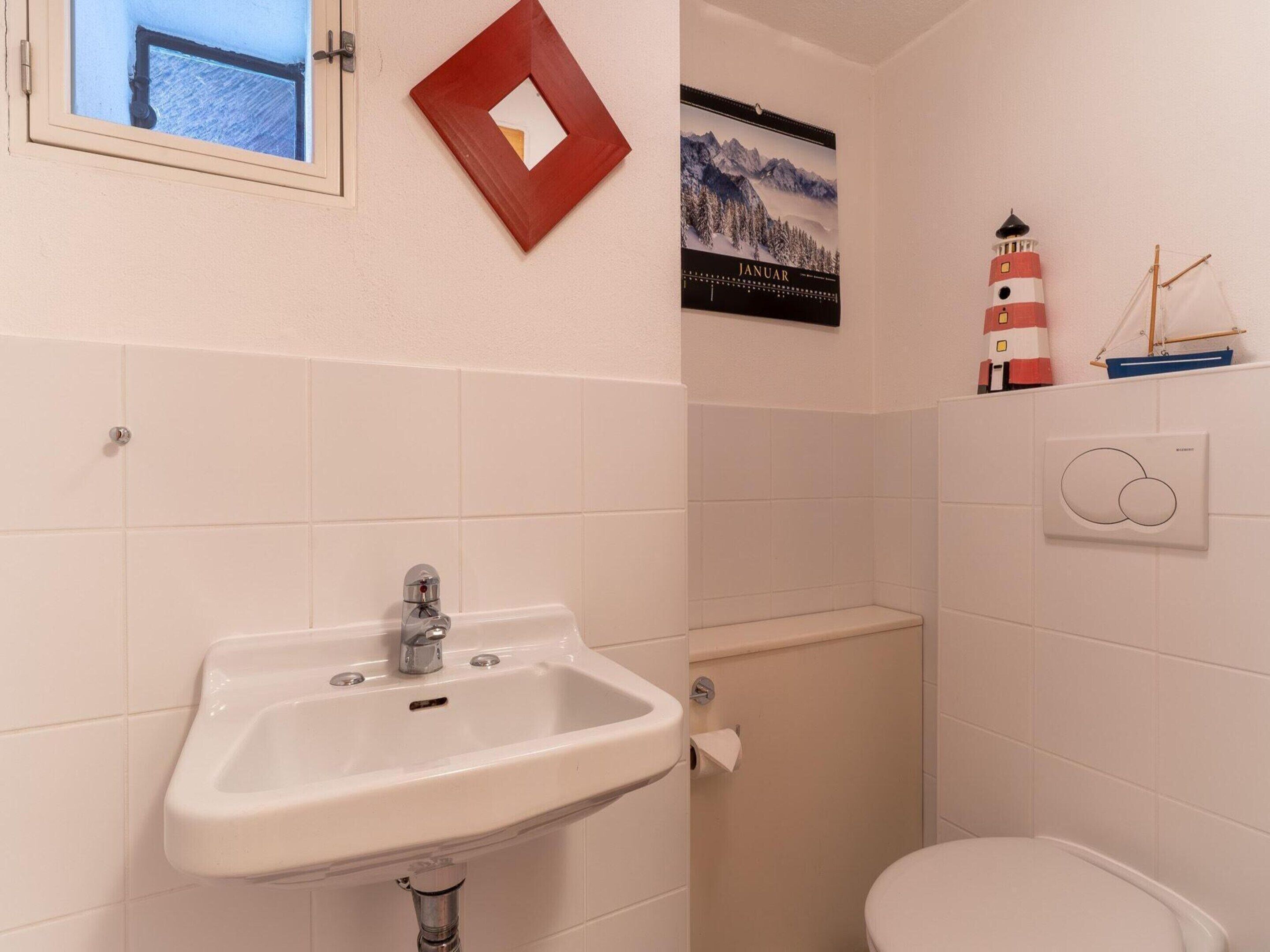 A bathroom with a white sink, toilet, and a small window. There is a poster on the wall and a small shelf with a model ship.