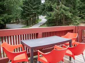 Une terrasse en bois avec une table et quatre chaises orange, entourée d’une rambarde rouge.