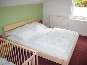 Un lit simple avec un cadre en bois, une literie blanche et un oreiller rouge.