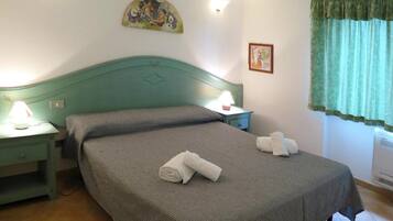 A room with a bed, two bedside tables, a lamp, a painting, a window with curtains, and an air conditioning unit.