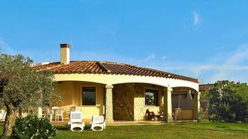 A house with a tiled roof, a covered patio, and a lawn with two white chairs.