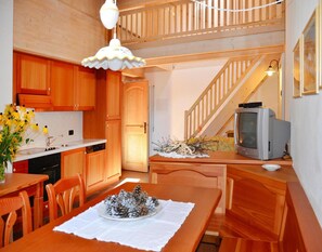 Een gezellige keuken met houten kasten, een eettafel met dennenappels, een oude televisie en een trap.