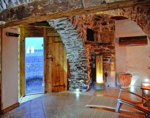 A rustic room with a wooden door labeled "Doccia," stone walls, a tiled floor, and a wicker chair. - Apartment in Pellizzano Near Shopping (Pellizzano)
