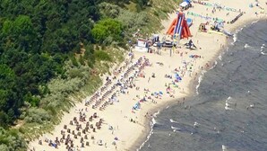 An aerial view of a beach with numerous sun loungers and umbrellas, a large inflatable slide, and a dense forested area to the left. - Apartment in Pellizzano Near Shopping (Pellizzano)