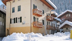A multi-story building with balconies, surrounded by snow-covered trees and a mountainous backdrop. - Apartment in Pellizzano Near Shopping (Pellizzano)