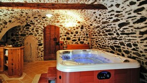 A stone-walled bathroom with a wooden bathtub, a wooden bench, and a shower area. - Apartment in Pellizzano Near Shopping (Pellizzano)