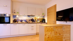 Una cucina moderna con mobili bianchi, un'isola in legno, forno integrato e televisore a schermo piatto.