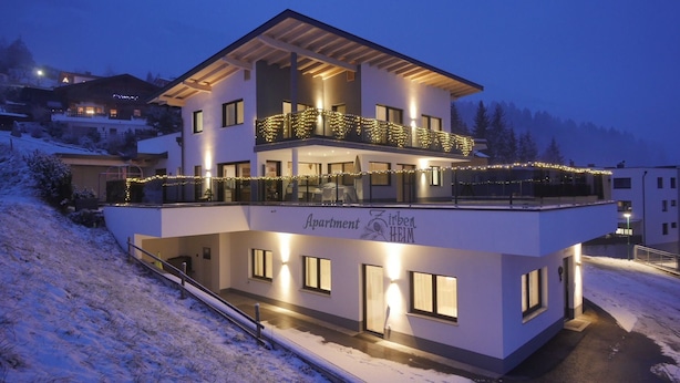 Un moderno edificio a due piani con un balcone decorato da luci a stringa, con l'indicazione "Apartment Zirben Heim".